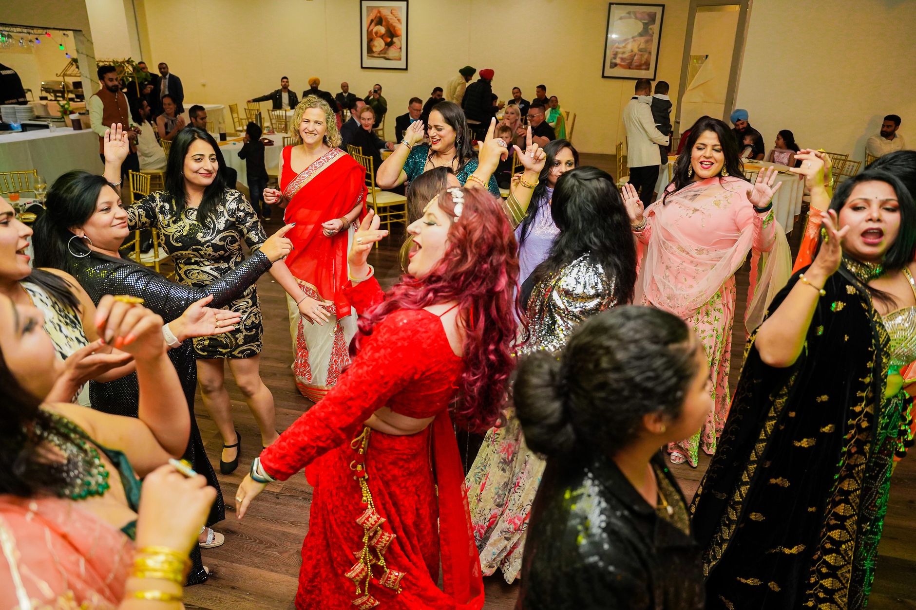 Women dancing joyfully at an Indian wedding party indoors, showcasing cultural attire and vibrant energy.