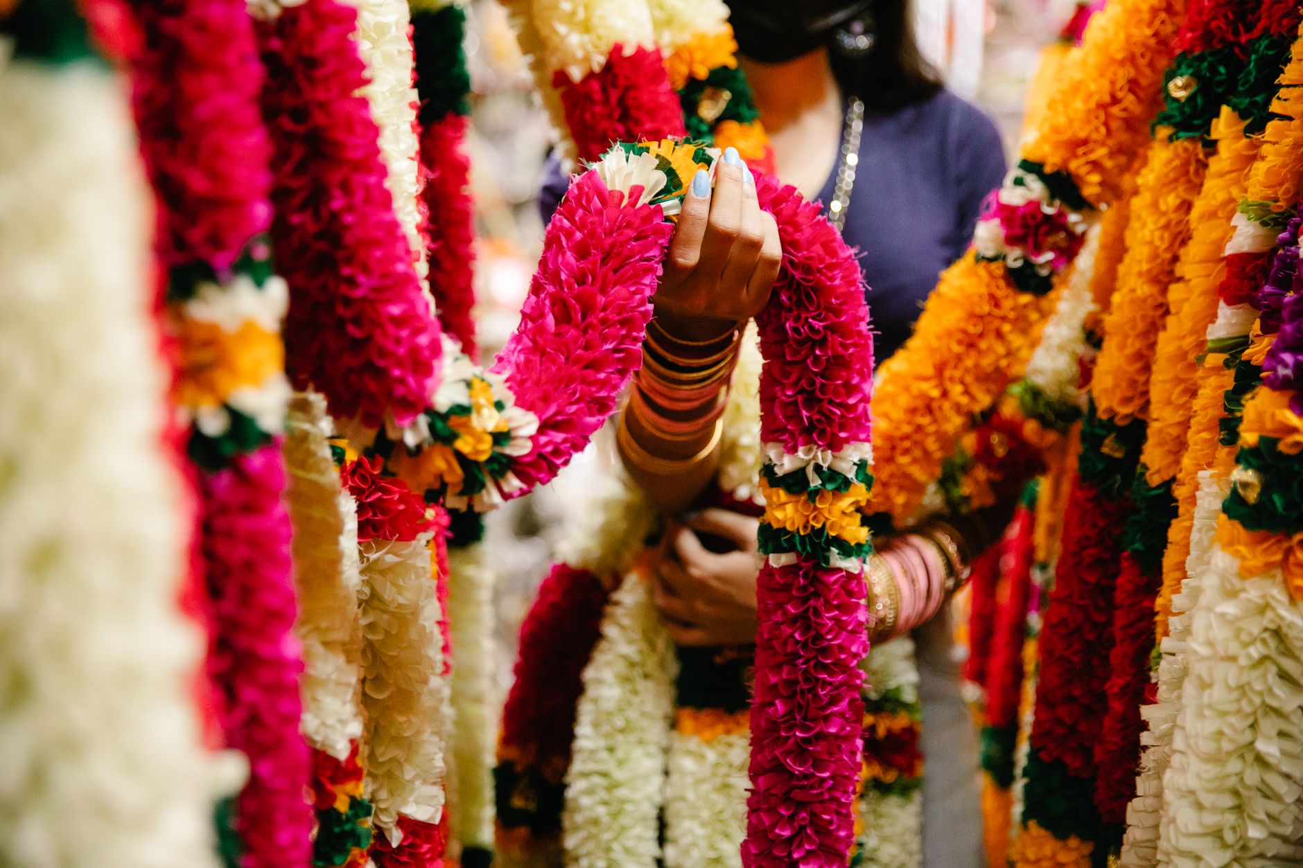 Colorful flower garlands being held by a woman in an Indian market, showcasing vibrant cultural decor.