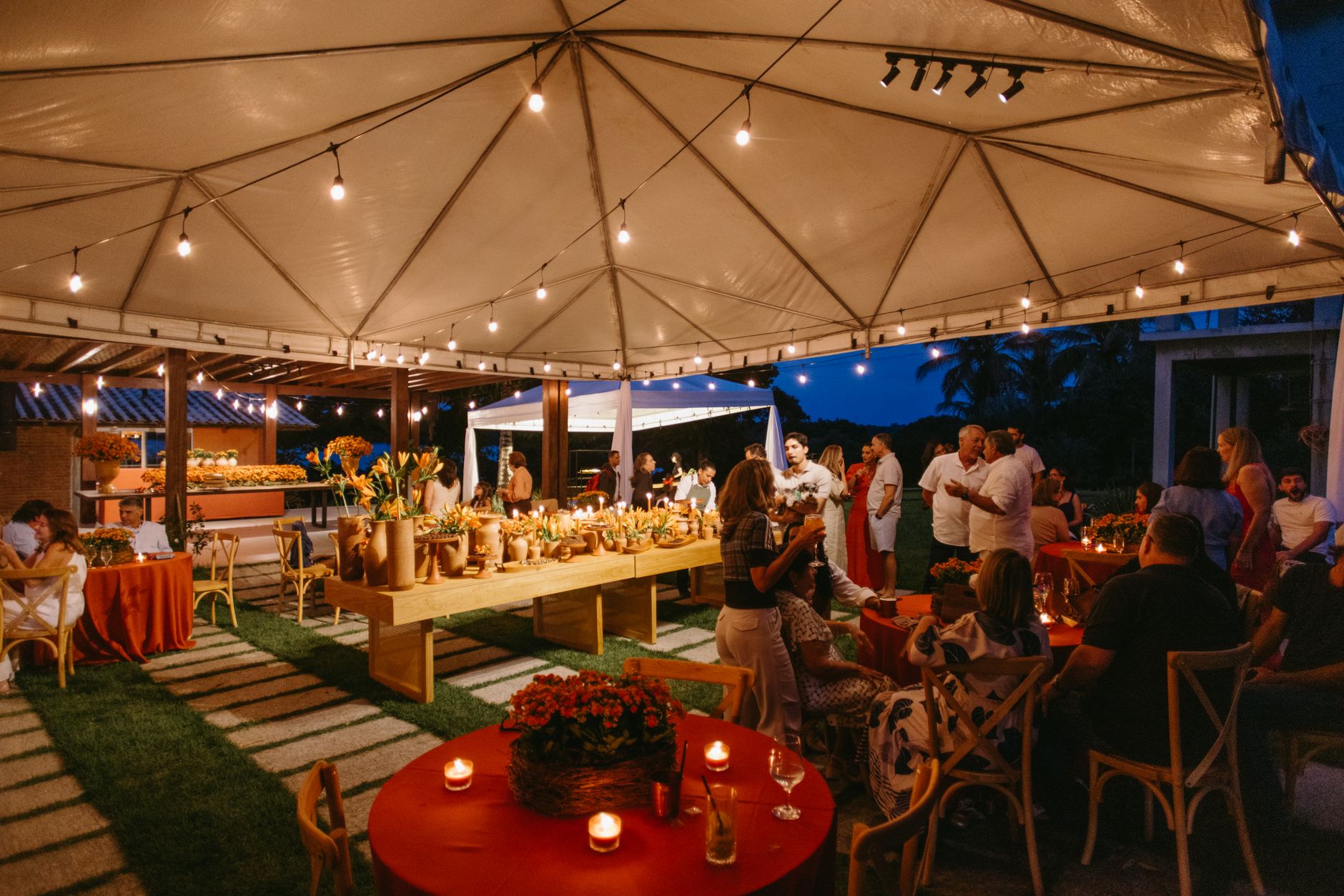 A beautifully decorated outdoor party under a tent with warm lighting.